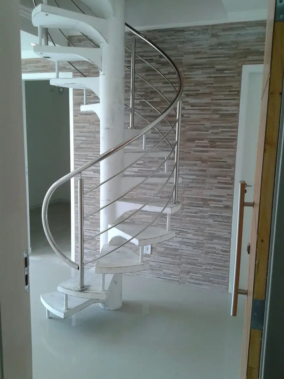 Escada caracol instalada em residência, com corrimão curvo em aço inox acompanhando os degraus