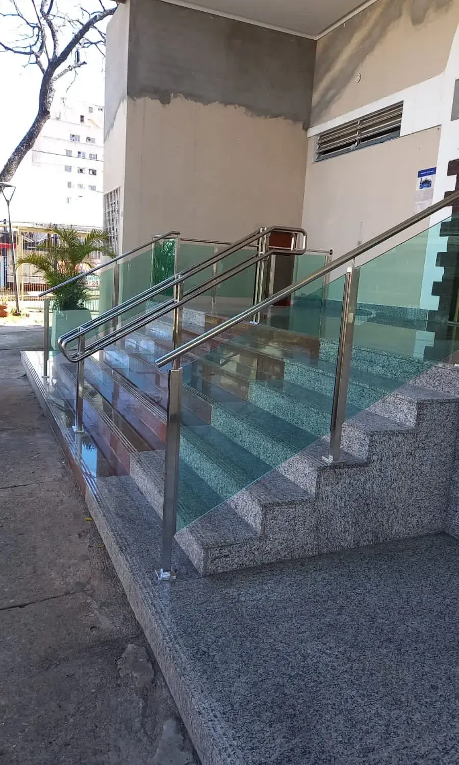Escada de acesso a edifício comercial protegida por guarda-corpo de vidro com montantes em aço inox